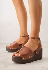Brązowe Sandały na Koturnie i Platformie Ozdobione Nitami Rhethe. Brązowe sandały Born2be, bez wzorów, z jeansu, eleganckie, bez obcasa, na koturnie, bez zapięcia. Za 99.99 zł.